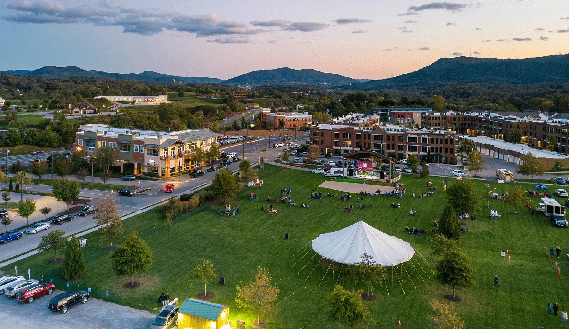 An aerial view of a community gathering with a stage, tents, and people enjoying an outdoor event at dusk.