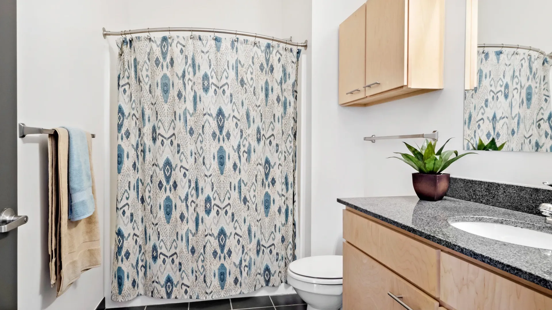 Bathroom with a patterned shower curtain, toilet, and vanity with a sink and granite countertop.