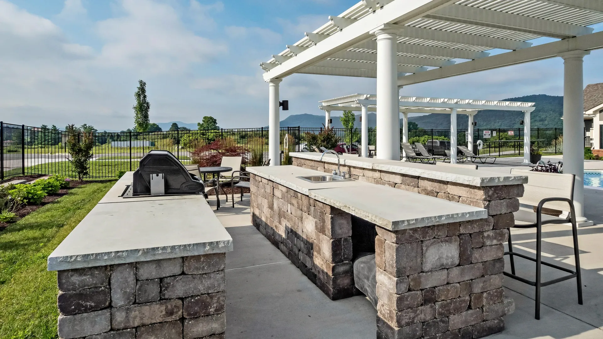 Outdoor kitchen with grill, sink, and counter space under a pergola.