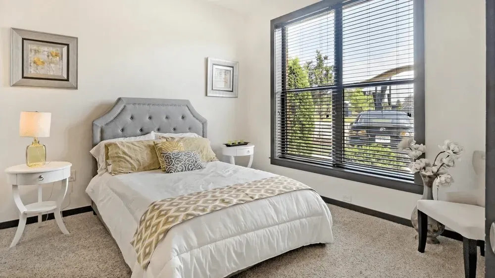 Bedroom with a queen-size bed, nightstand with lamp, and a large window.