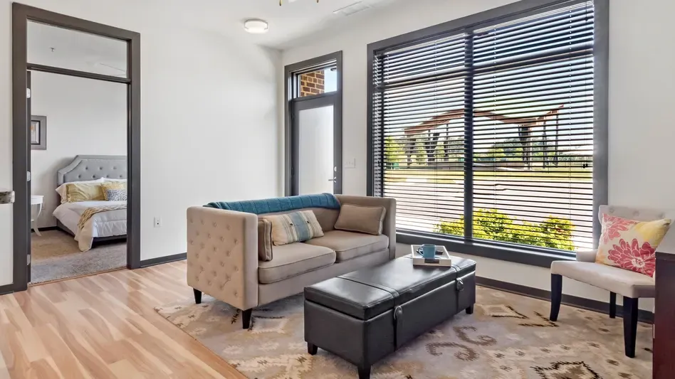 Living room with couch and ottoman, bedroom visible through doorway.