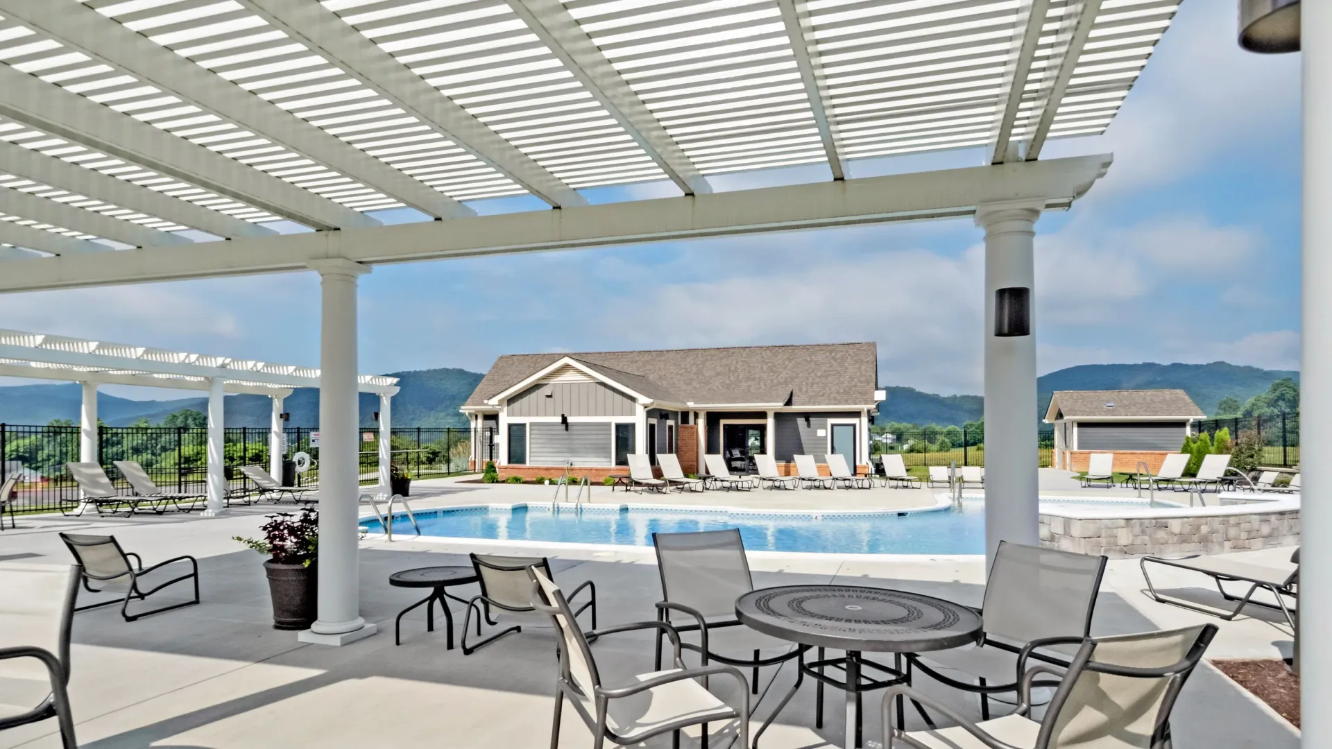 Outdoor swimming pool area with lounge chairs, tables, and a clubhouse in the background.