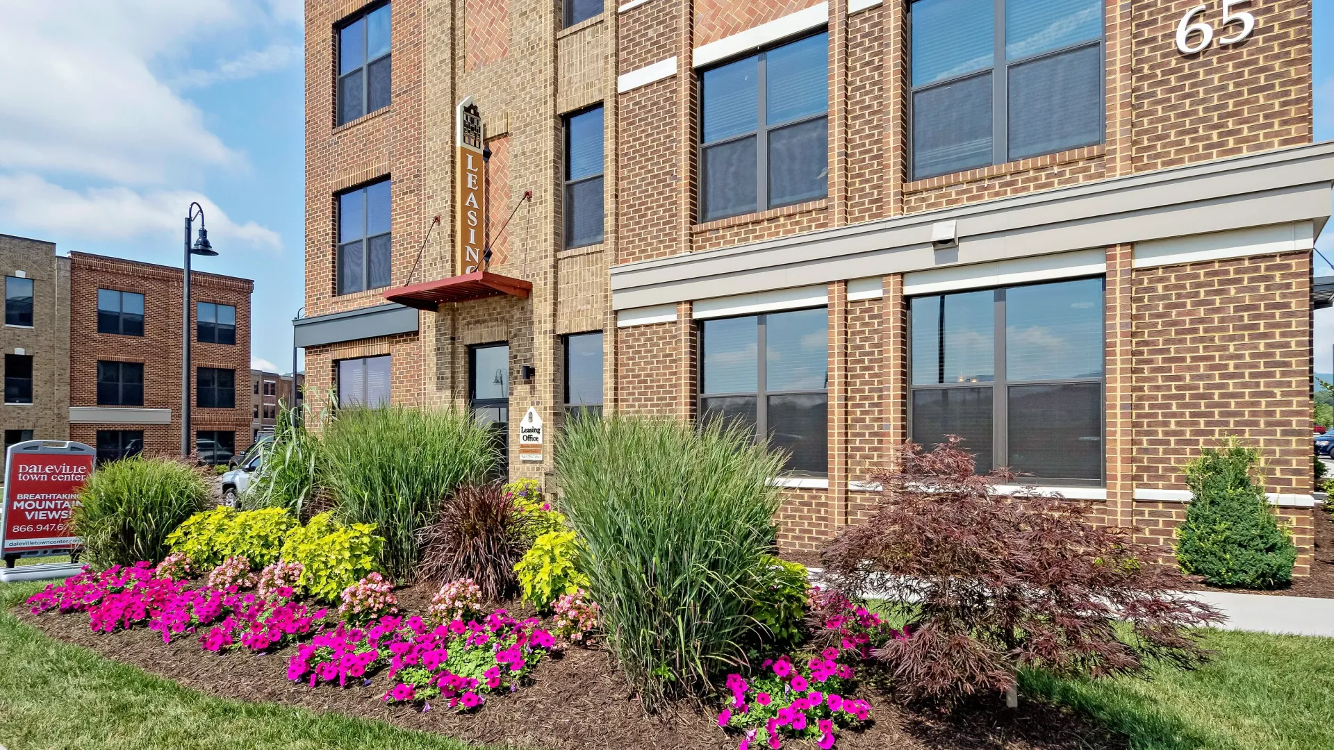 Exterior of brick apartment building with lush landscaping and signage.