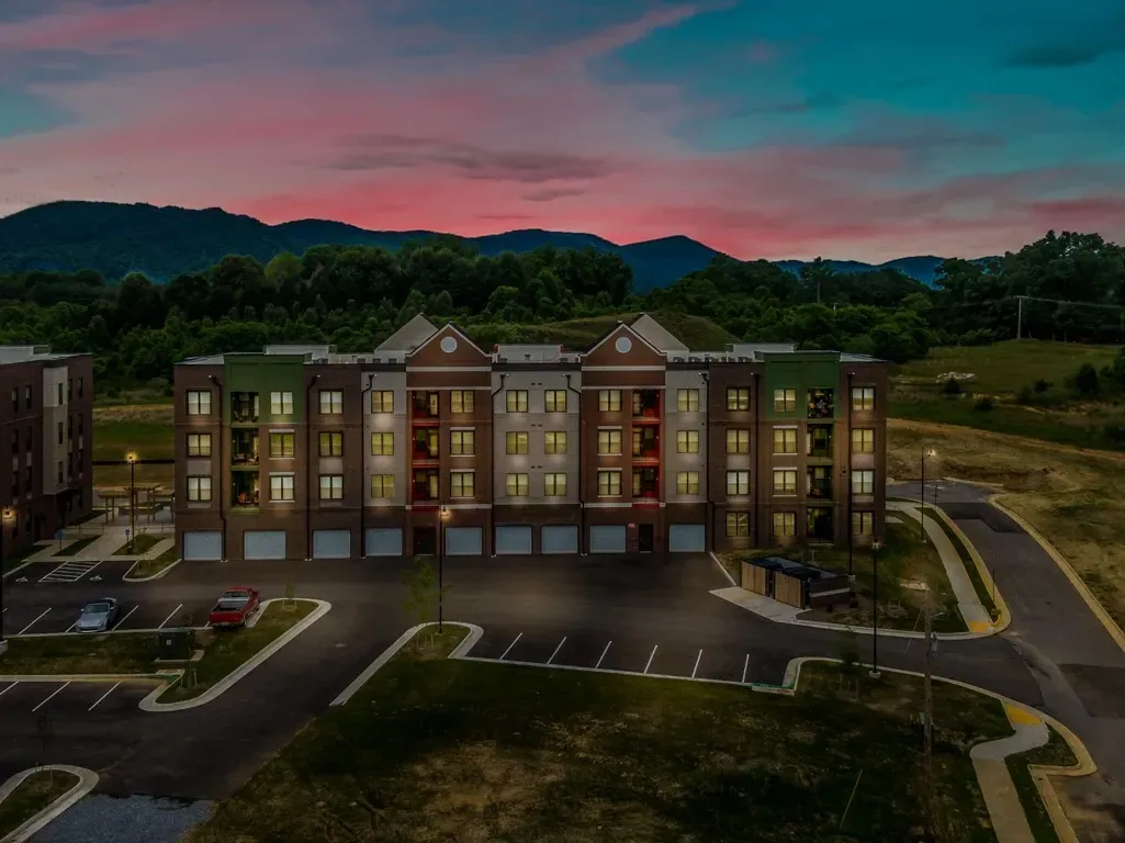 Exterior view of a modern apartment building at dusk with mountains in the background.