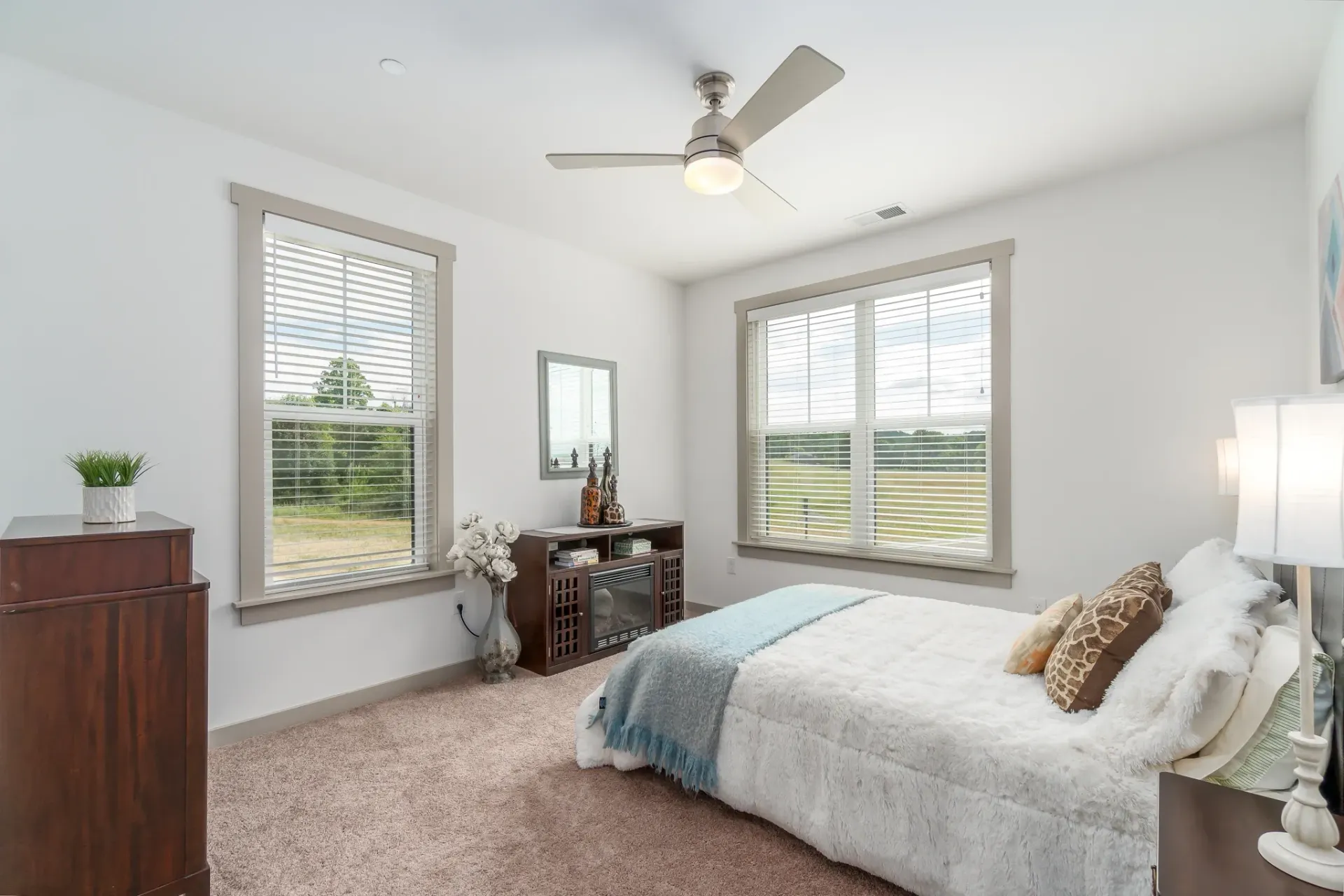 Cozy bedroom with a queen-size bed, ceiling fan, electric fireplace, and scenic views from the windows.