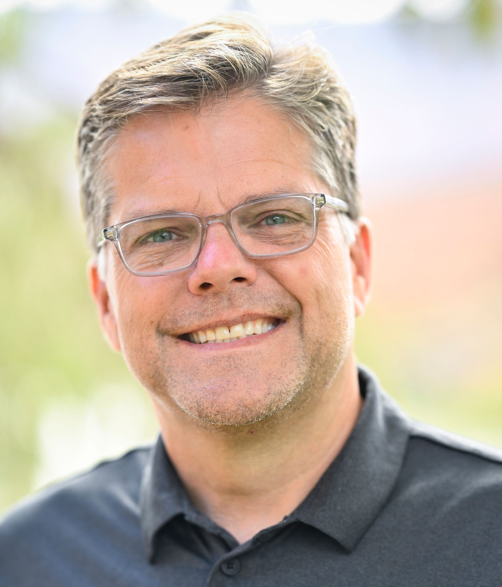 Man wearing glasses and a green zip-up sweater smiles at the camera against a blue background.