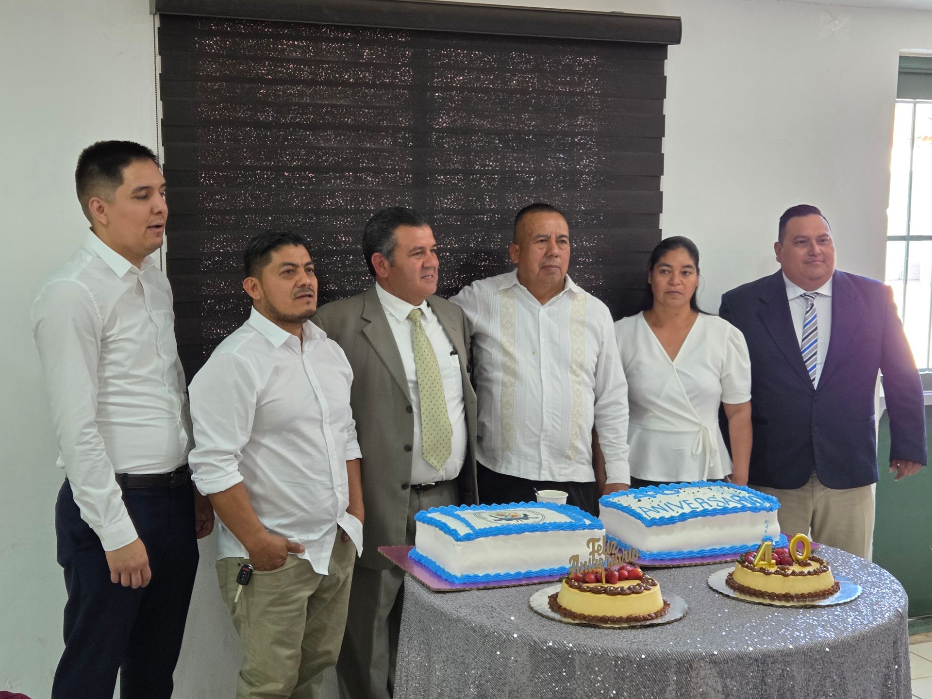 Group of people pose with cakes, celebrating an event in a room.