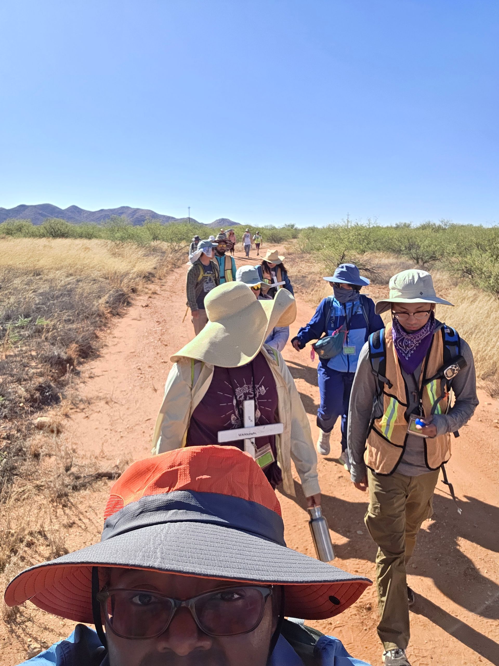 Group of people hiking on a dirt path in a desert landscape under a clear blue sky.