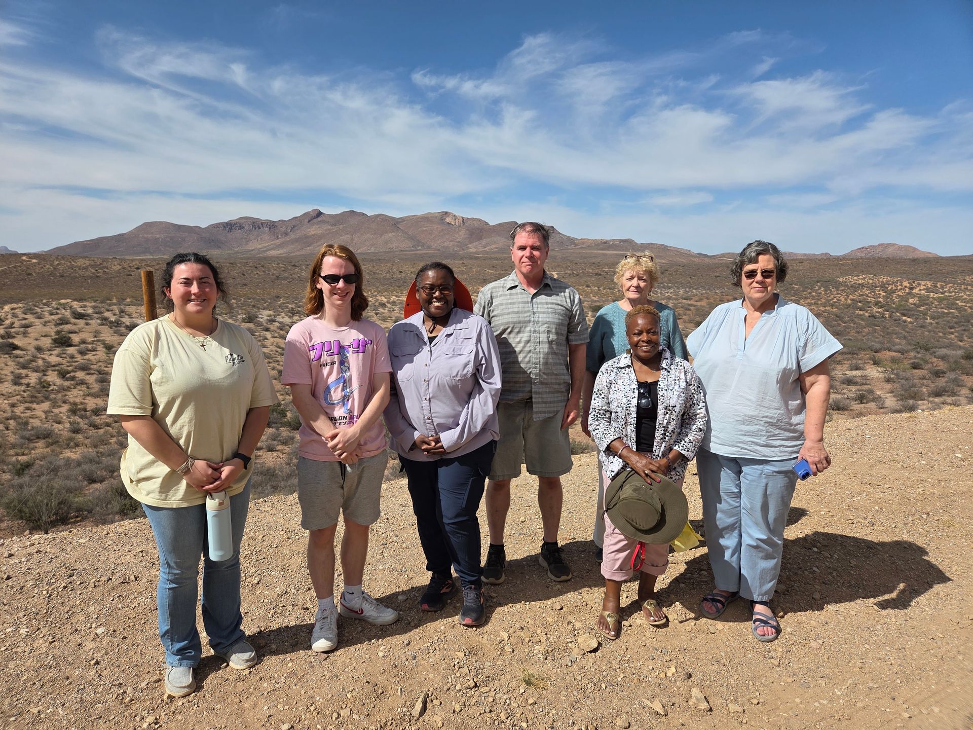 Group of people posing outdoors in a desert landscape under a blue sky.
