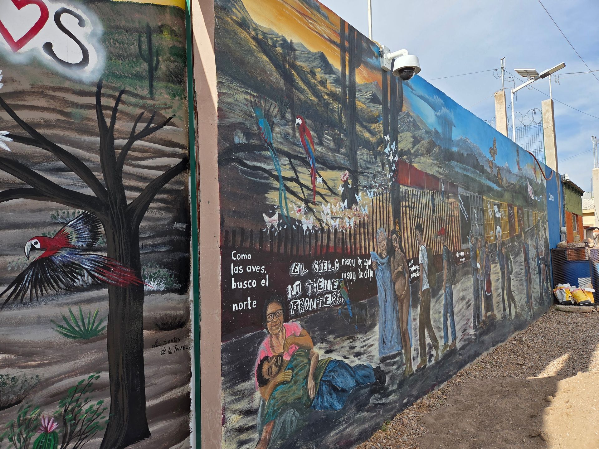 Colorful mural on a wall depicting a landscape, figures, and birds along a narrow street.