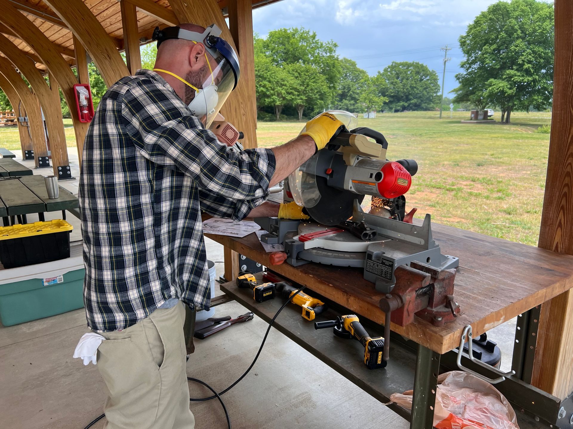 Man wearing safety gear using a circular saw outdoors at a wooden picnic table.