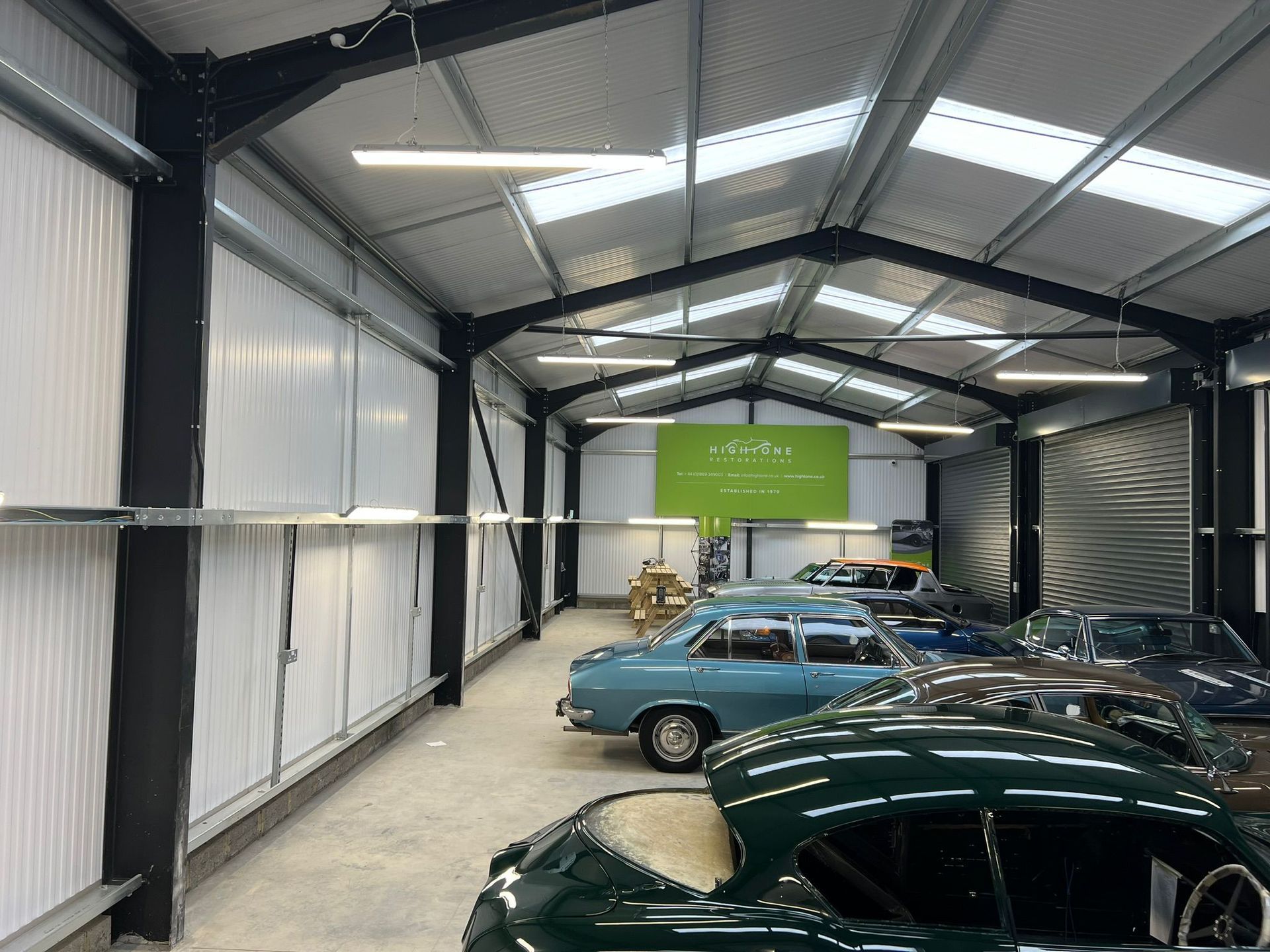 A spacious warehouse garage with several vintage and classic cars parked inside under high, bright interior lighting.