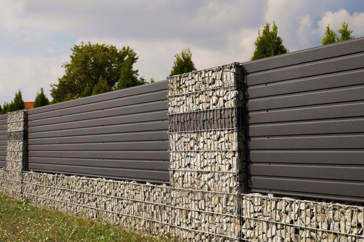 A modern fence featuring dark horizontal slats alternating with stone-filled gabion pillars and a low gabion base.