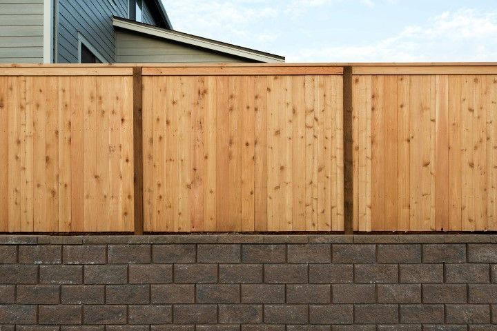 A wooden privacy fence mounted on top of a gray concrete block retaining wall.