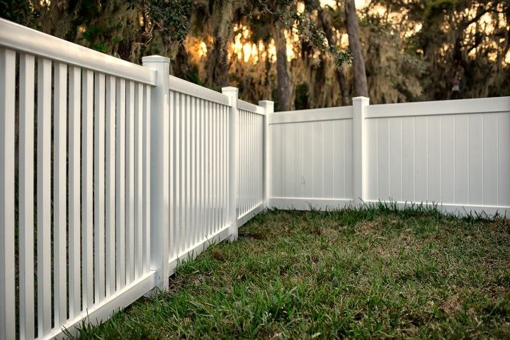 A white vinyl fence with alternating picket and solid panels enclosing a grassy yard at dusk.