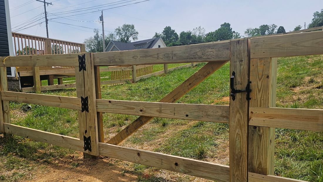 A wooden gate with black hinges and a latch installed in a fenced backyard on a sunny day.