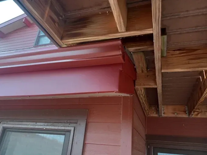 Red gutters and trim on a house corner with exposed wooden beams overhead; exterior view.