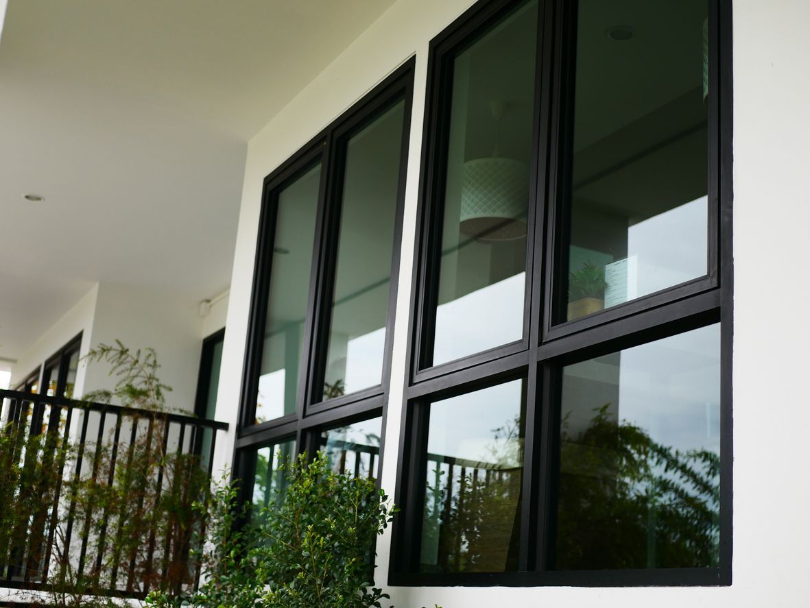 Black-framed windows on a white building exterior. Reflecting green foliage and a balcony.