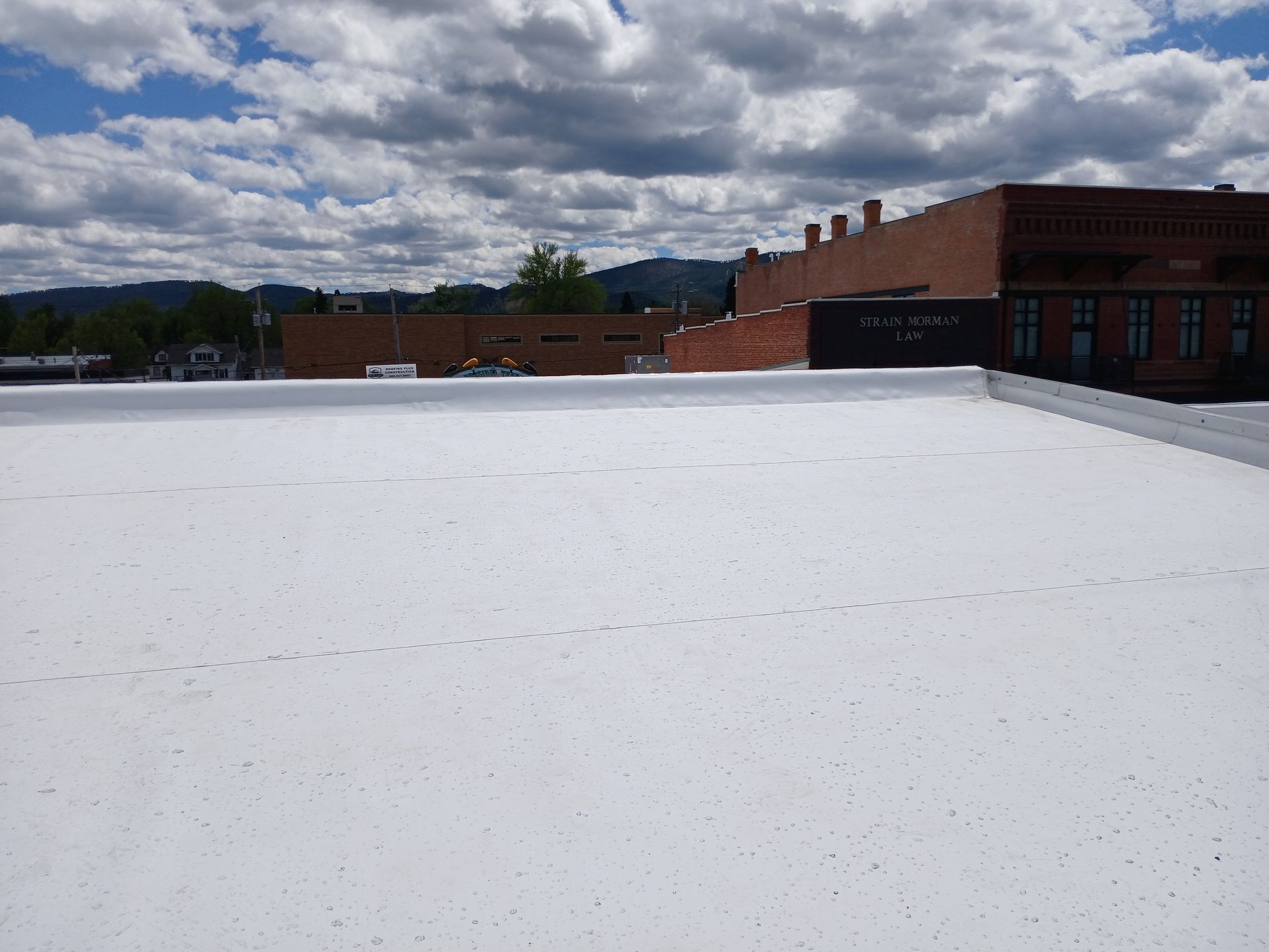 Rooftop with HVAC units. Gray metal boxes and vent on white roofing. Sunny day.