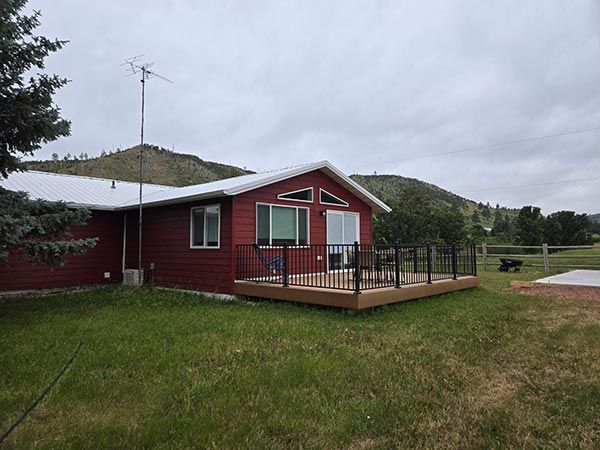 Red cabin with deck, antenna, and mountains in the background on a cloudy day.