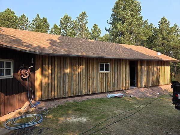 A building with new vertical wood siding. Brown shingles and trees in the background.