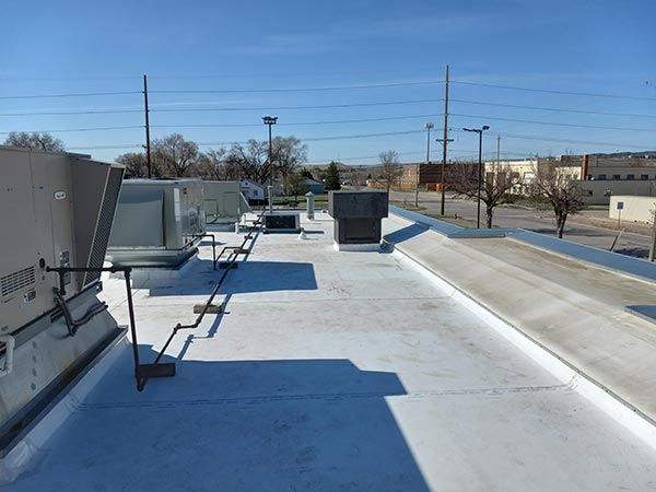 A white commercial roof with HVAC units and a ladder, under a clear, blue sky.