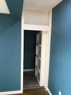 Narrow hallway with blue walls and a white doorway leading to a closet with shelves.