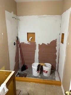 Small bathroom under renovation with patched walls, tools, buckets, and a mop on the floor.