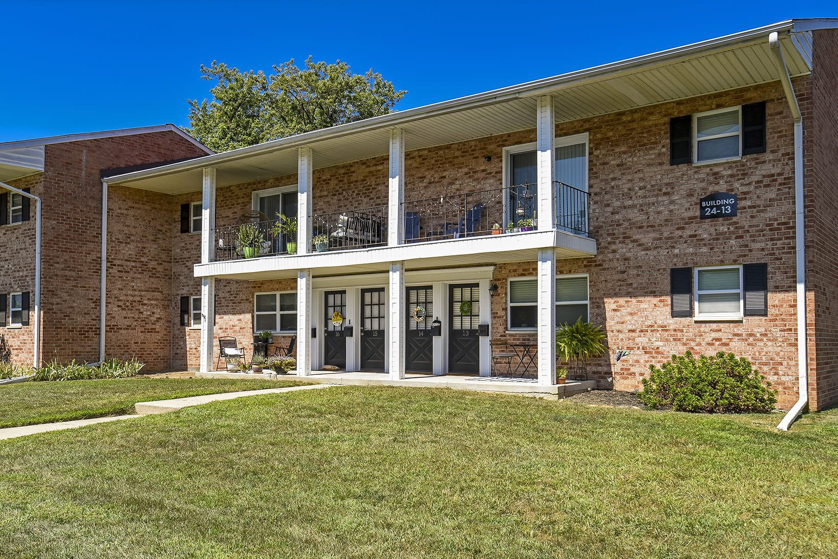 Two-story brick apartment building exterior with doors, balconies, and a green lawn at Holly Court, offers apartments in Pitman, NJ.