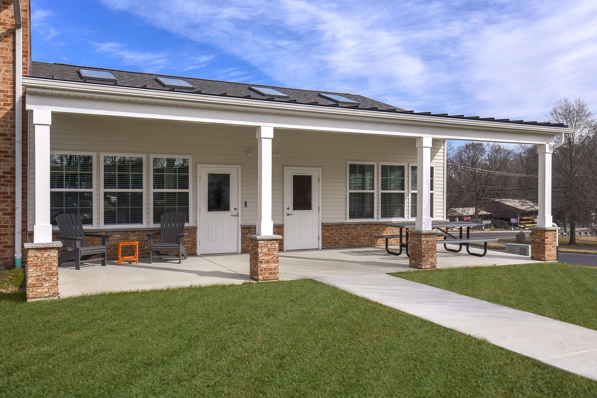 Covered front porch of an apartment building with white columns, brick bases, and outdoor seating at Holly Court, offers apartments in Pitman, NJ.