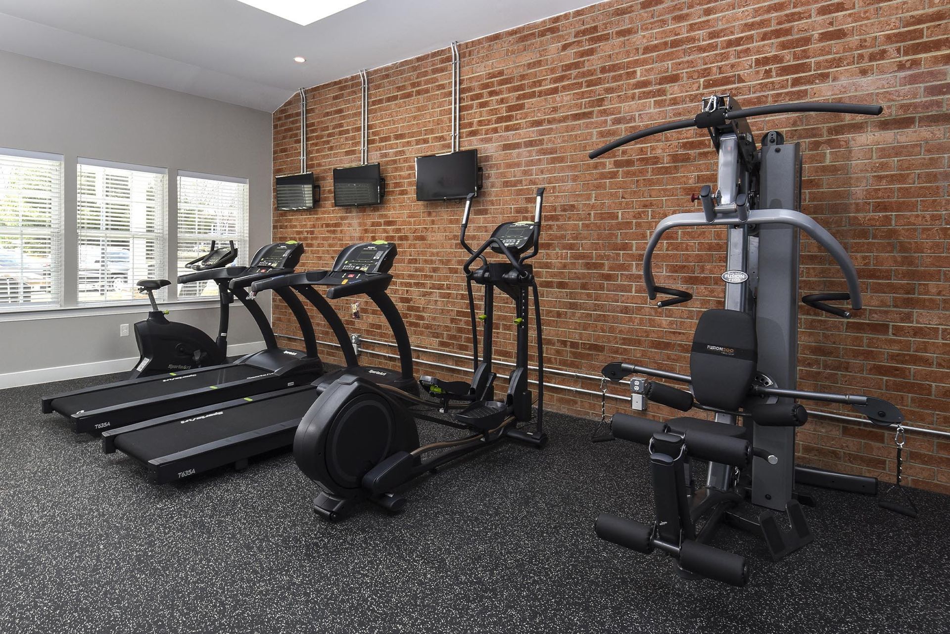 Fitness center with treadmills, elliptical, and weight machines against a brick wall at Holly Court, offers apartments near Rowan University.