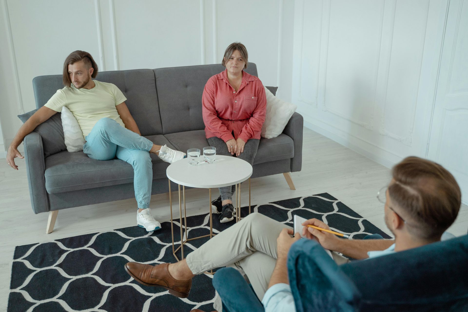 Couple sitting on a couch in therapy session with counselor taking notes.