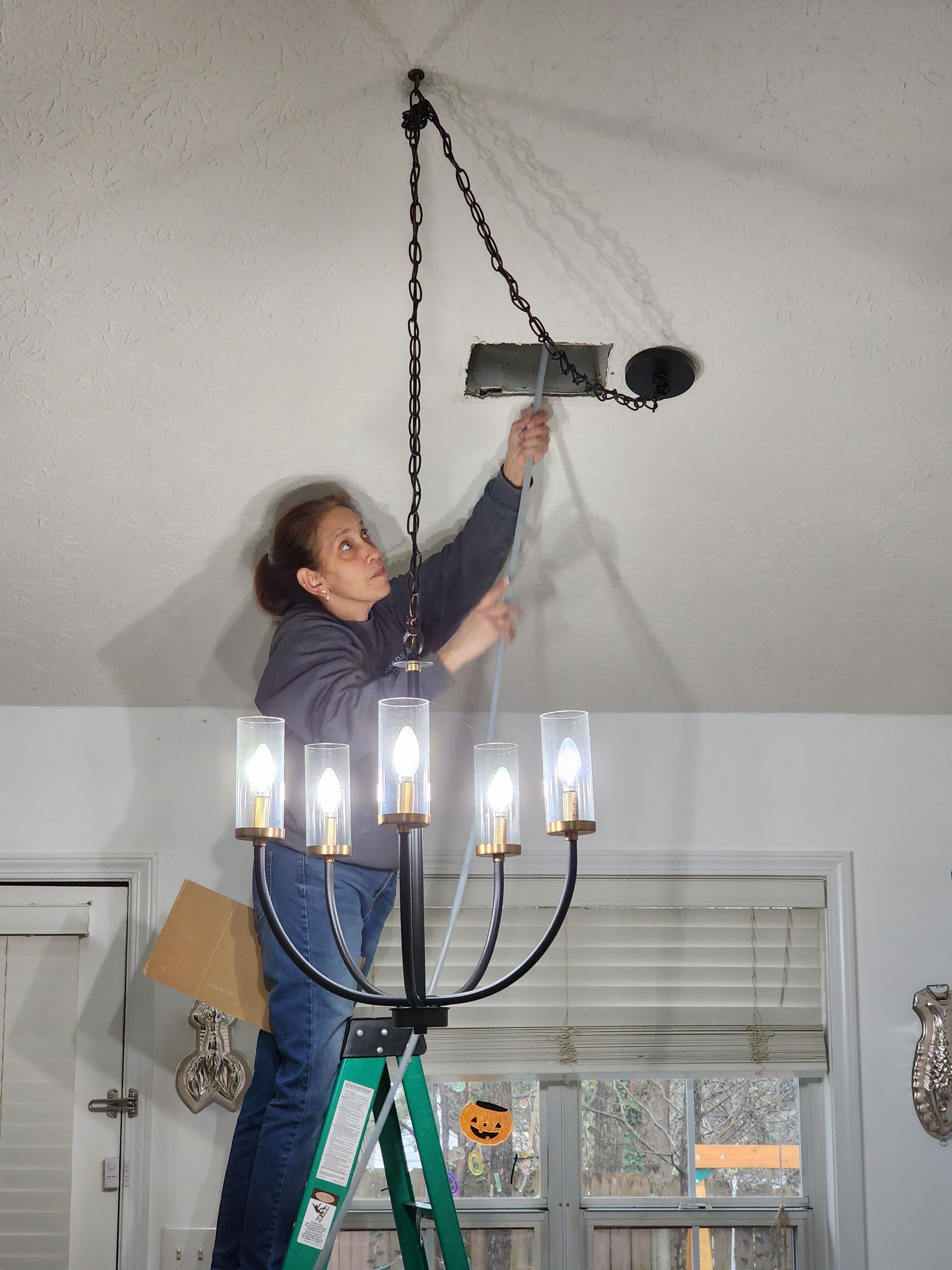 A woman is standing on a ladder working on a chandelier