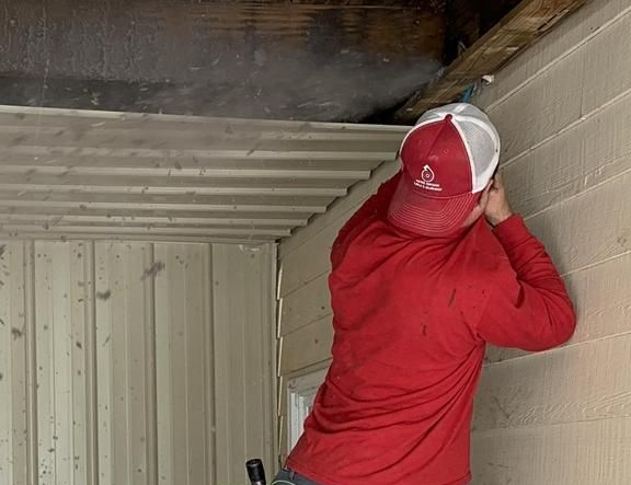 A man is standing on a ladder cleaning an air vent.
