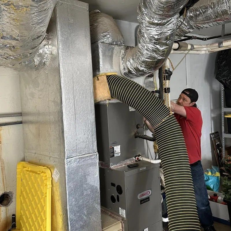 Technician inspecting HVAC ductwork in a basement with insulated silver vents and a yellow portable fan