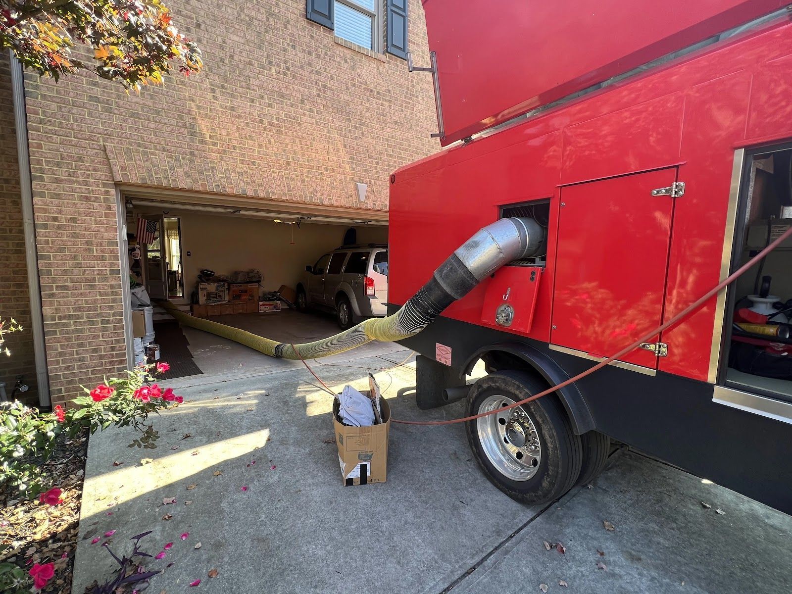Red vacuum hose from truck clearing debris from a brick garage driveway
