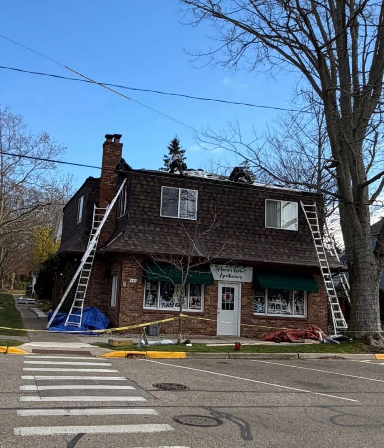 Small brick storefront on a corner with ladders leaned against both sides and a crosswalk in front.
