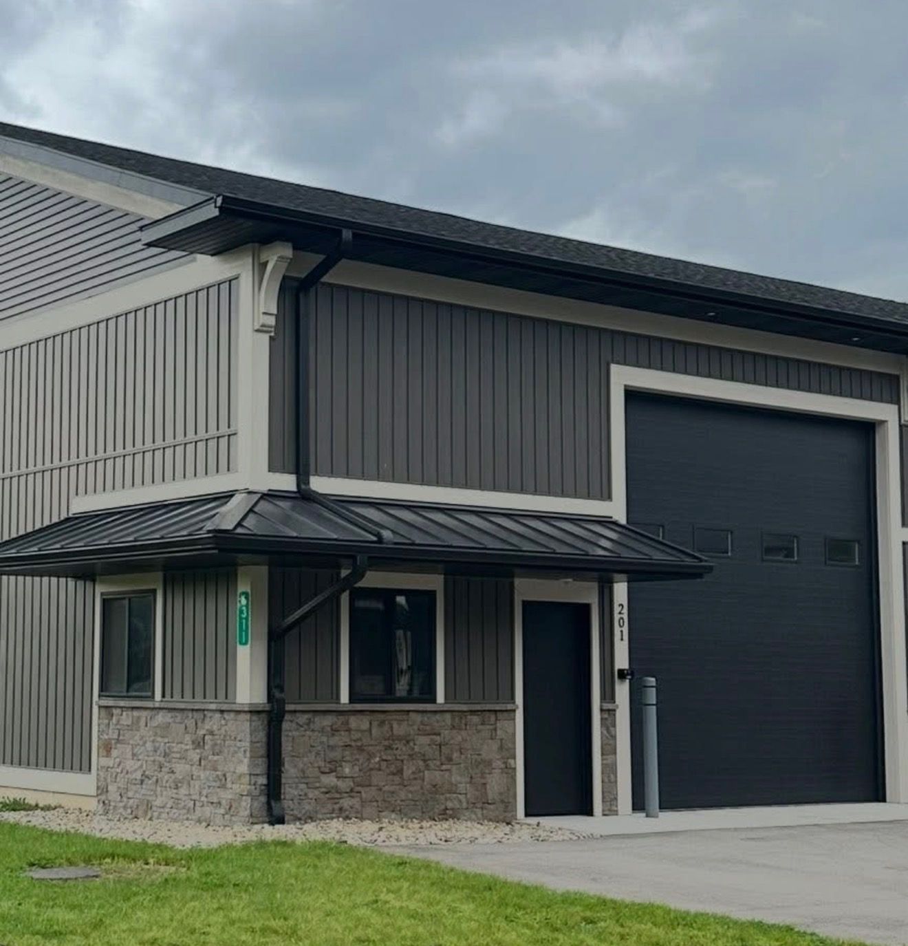 Modern gray industrial building with metal siding, stone base, and a large black garage door