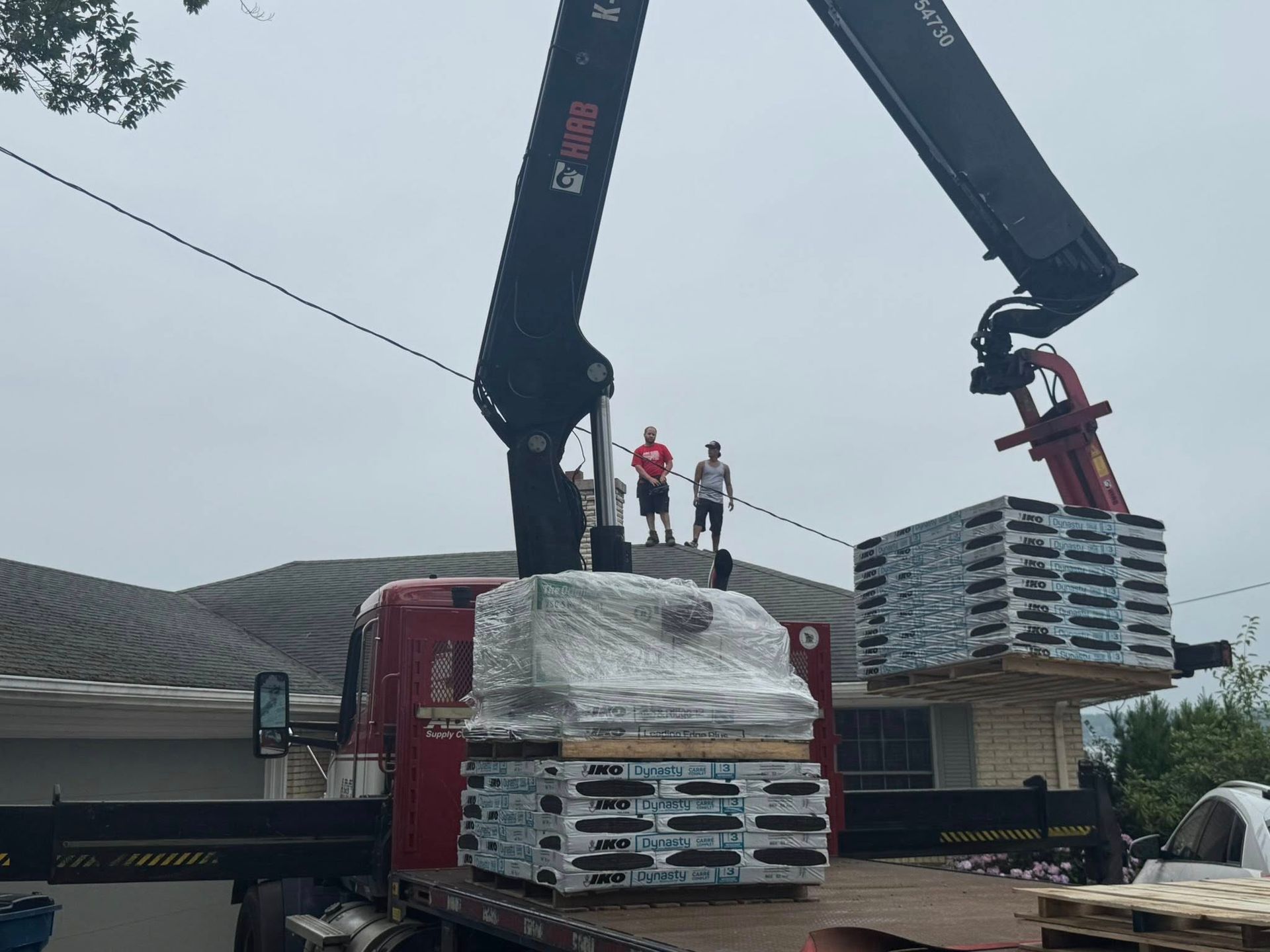 Crane unloading stacked pallets at a building site, with two workers standing on a wrapped pallet.