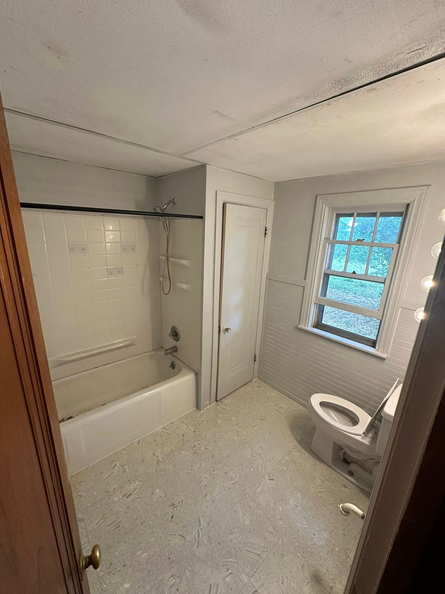 Small bathroom with white tub, toilet, tiled floor, and window with bars; under renovation.