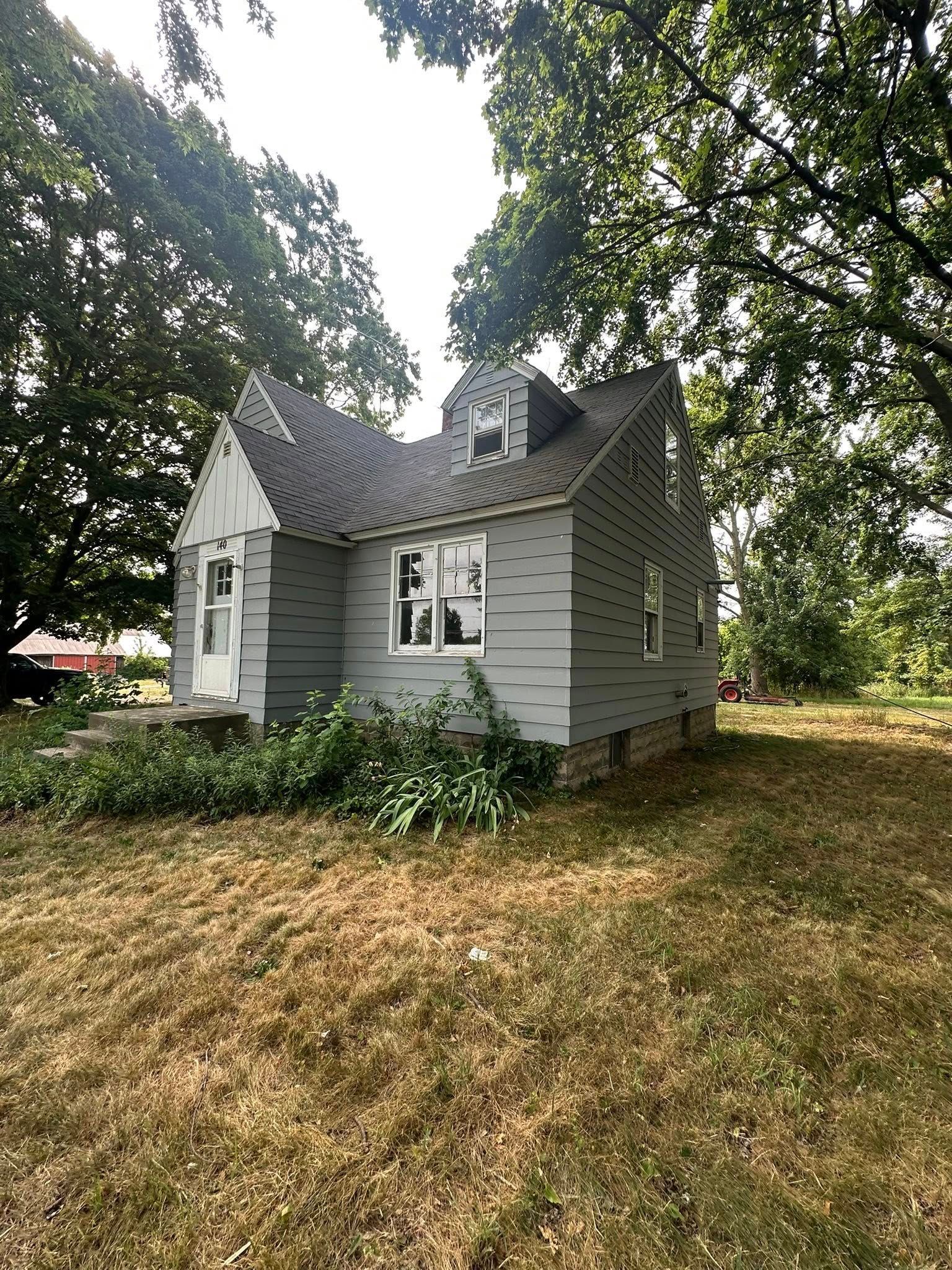 Small gray house with a steep roof, surrounded by trees and dry grass.