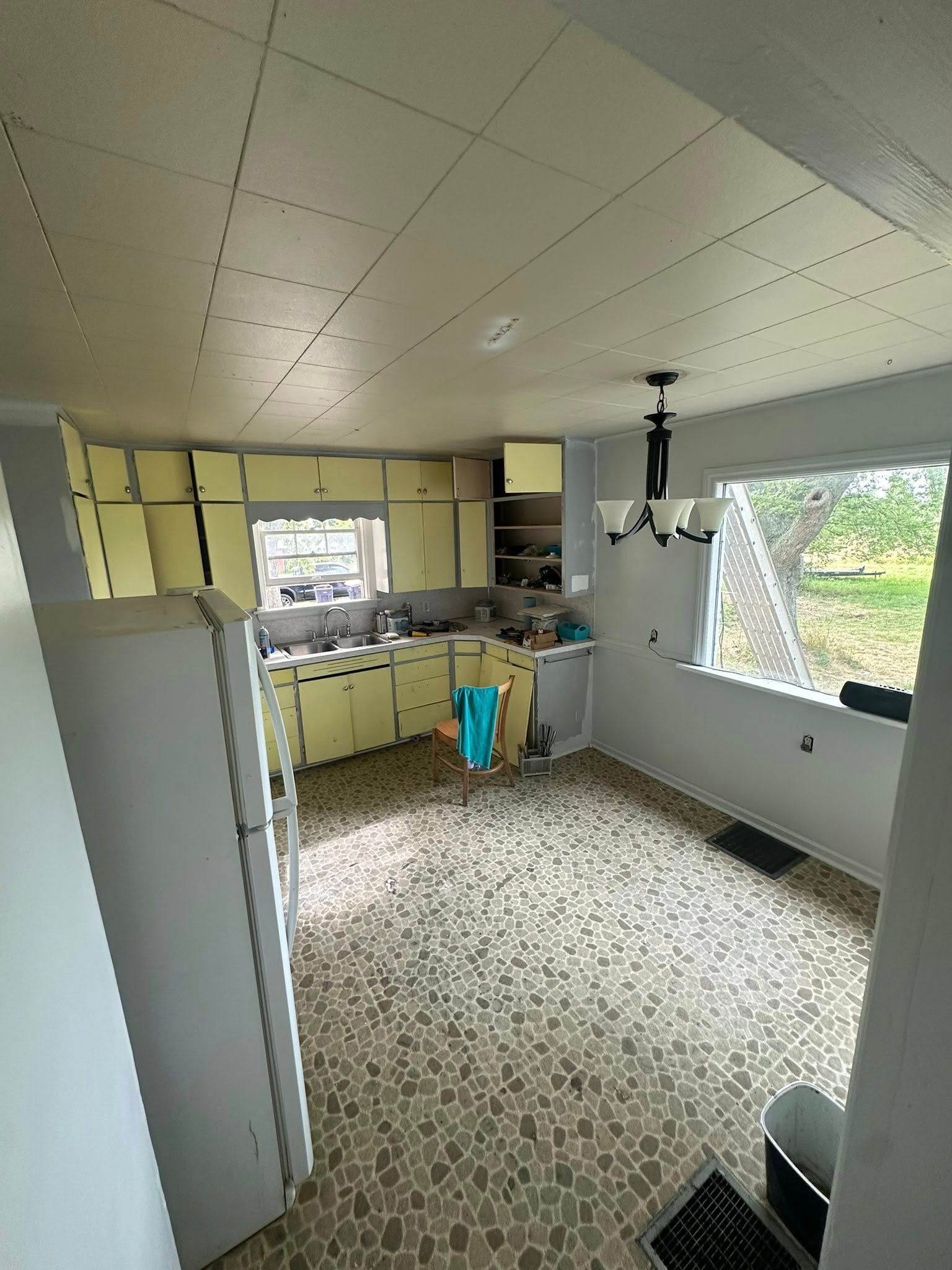 Small kitchen with white cabinets, patterned floor, open window, and daylight coming in.