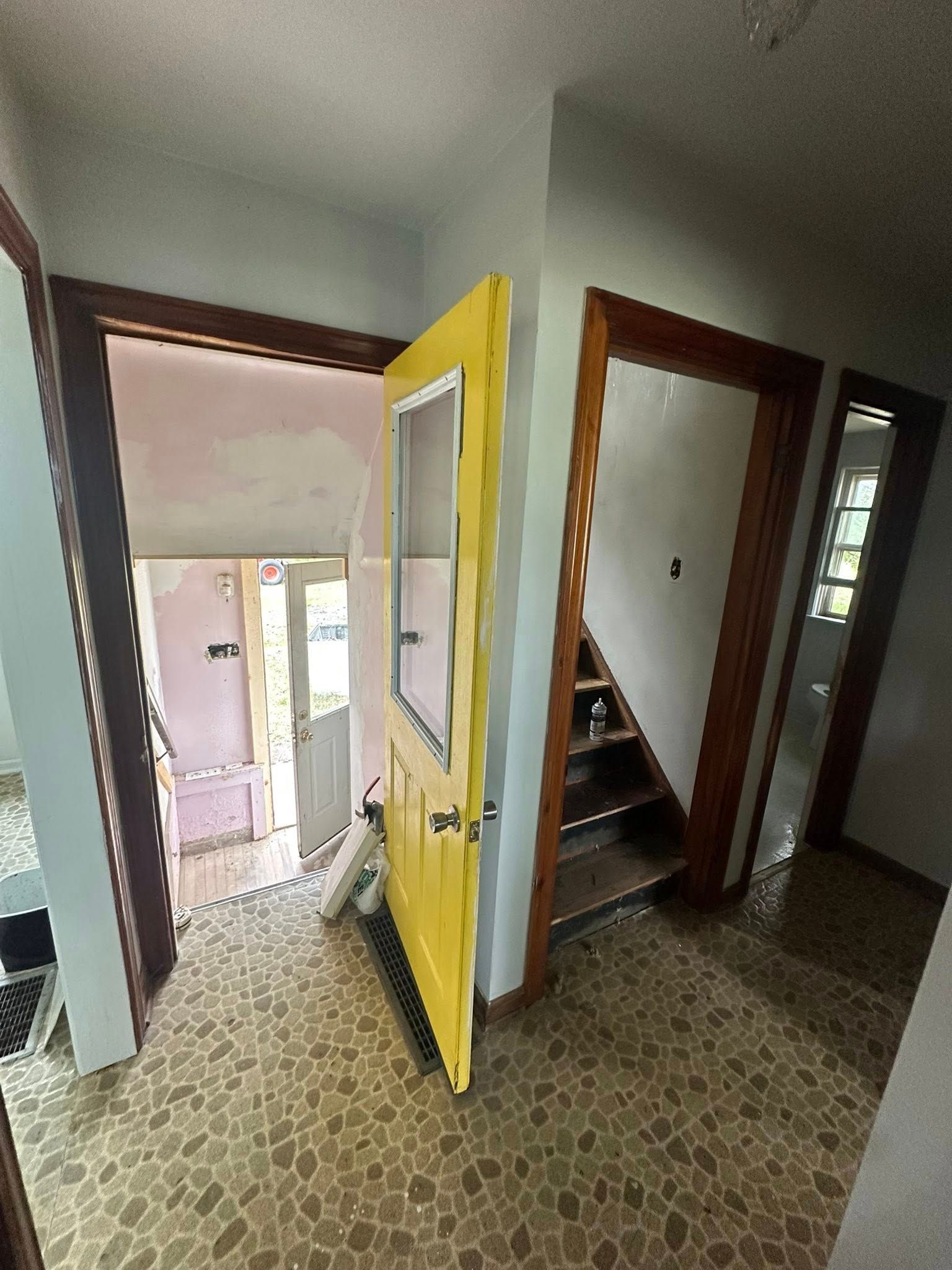 Hallway with open yellow door, patterned tile floor, and staircase beside a doorway
