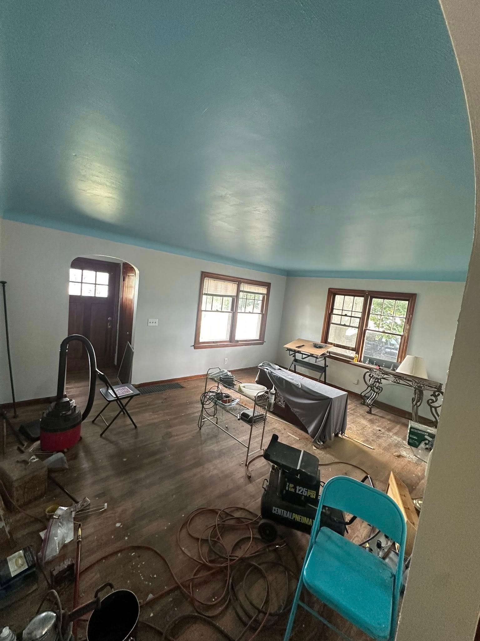 Empty room with blue walls and ceiling, windows, scattered chairs, cables, and a keyboard.