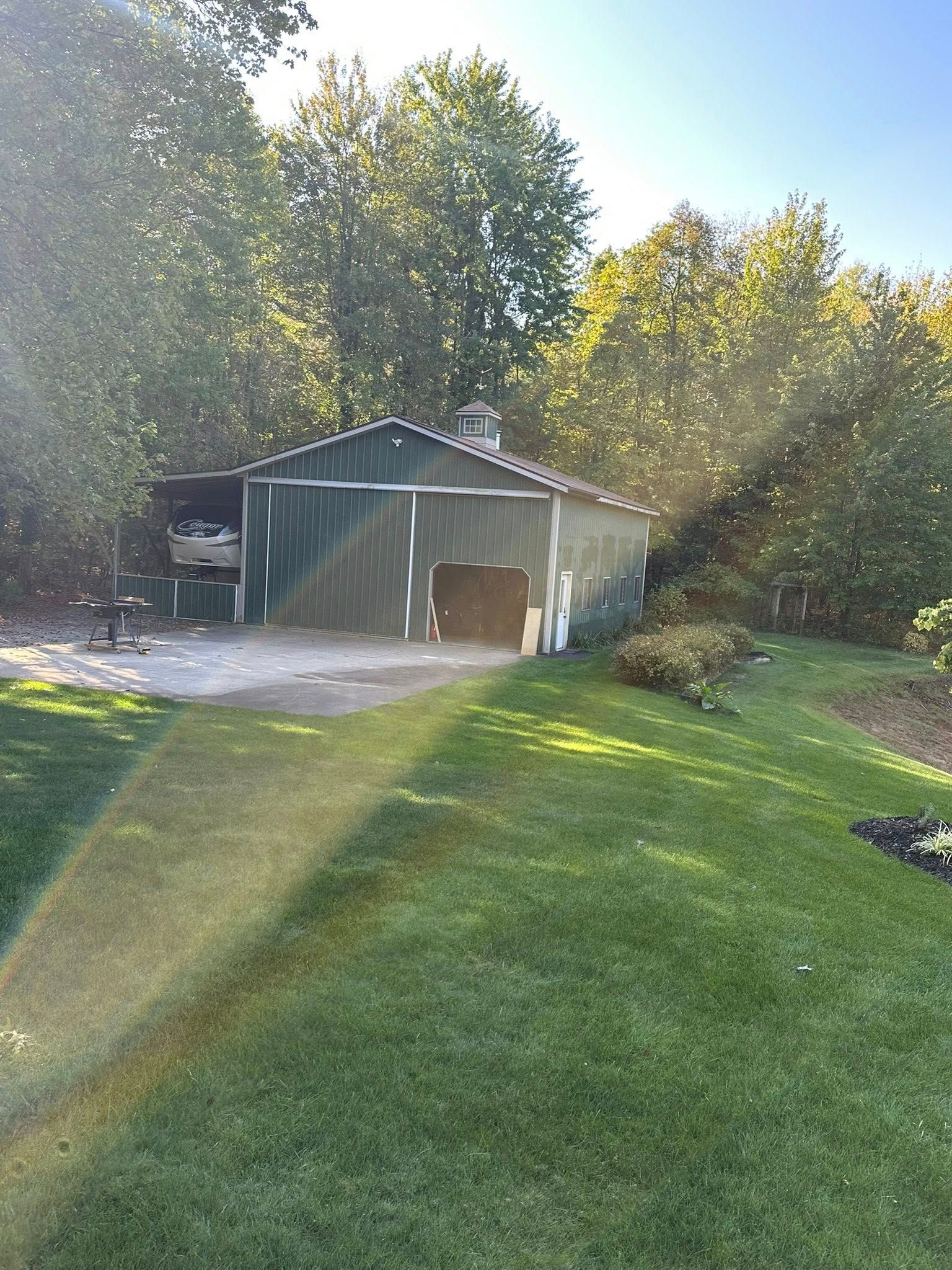 Sunlit backyard with a green shed, garage door, lawn, and trees in the background.