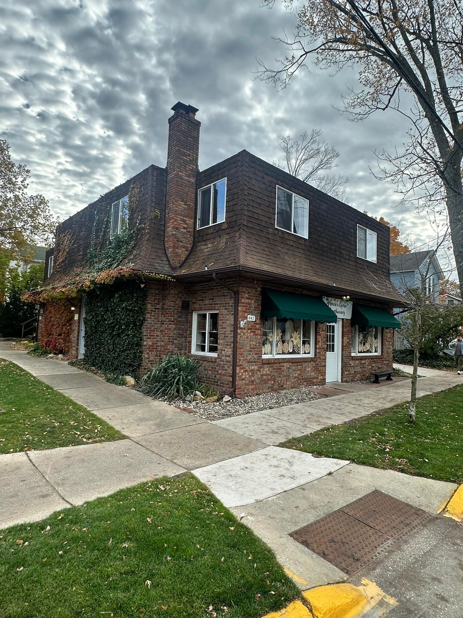 Brick corner building with brown shingled roof, chimney, and green awning on a cloudy day