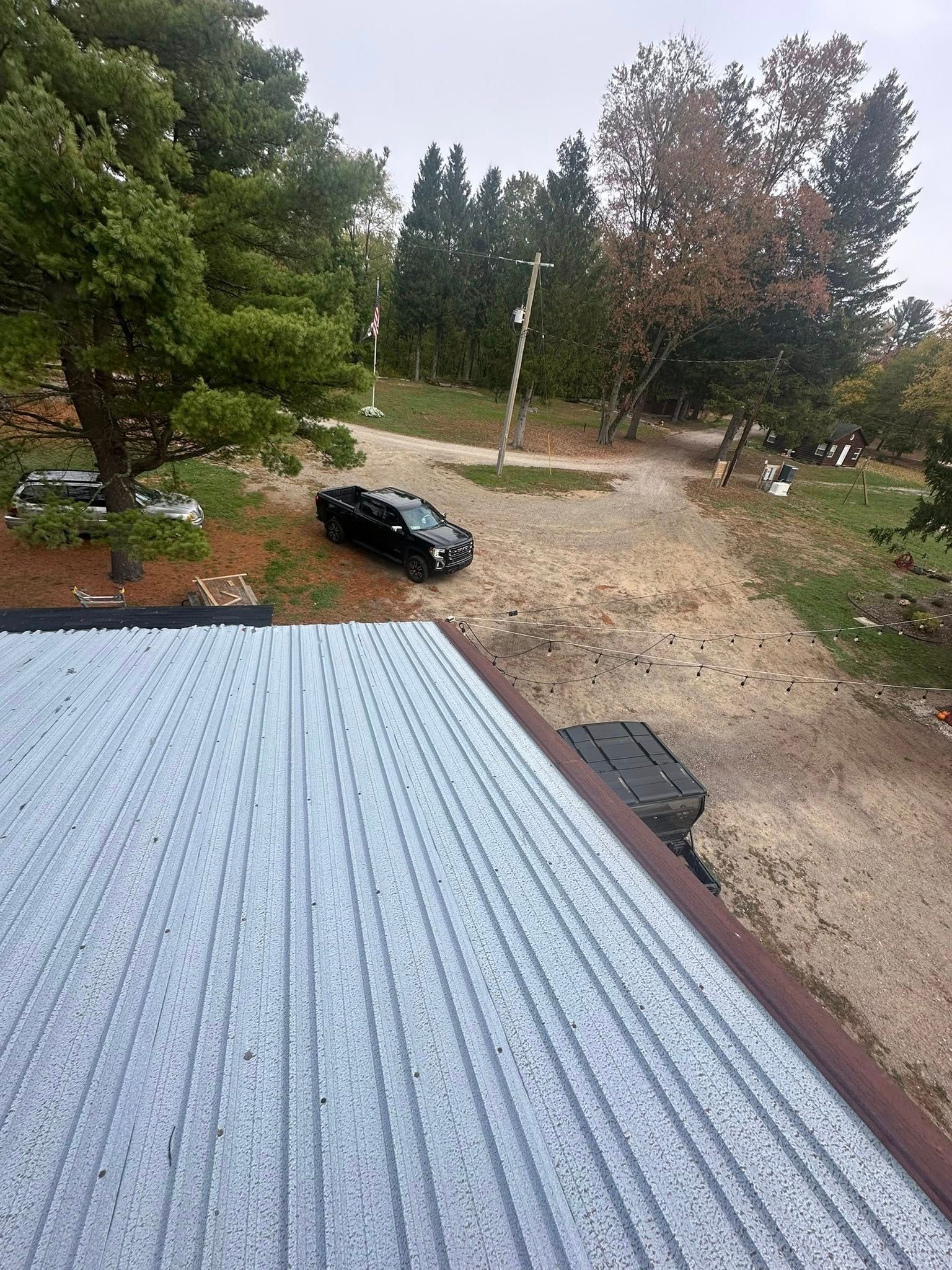 View from a roof over a gravel yard with trees, a parked black car, and overcast sky.