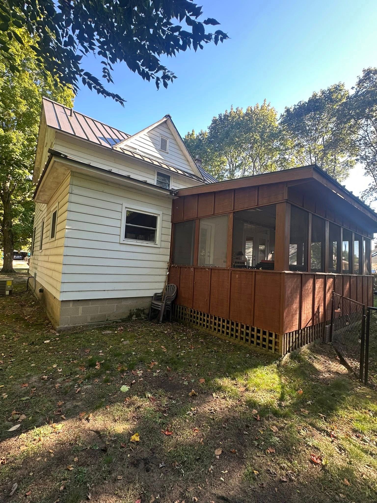 Small white house with a screened porch and red railing, viewed from a grassy yard under trees.