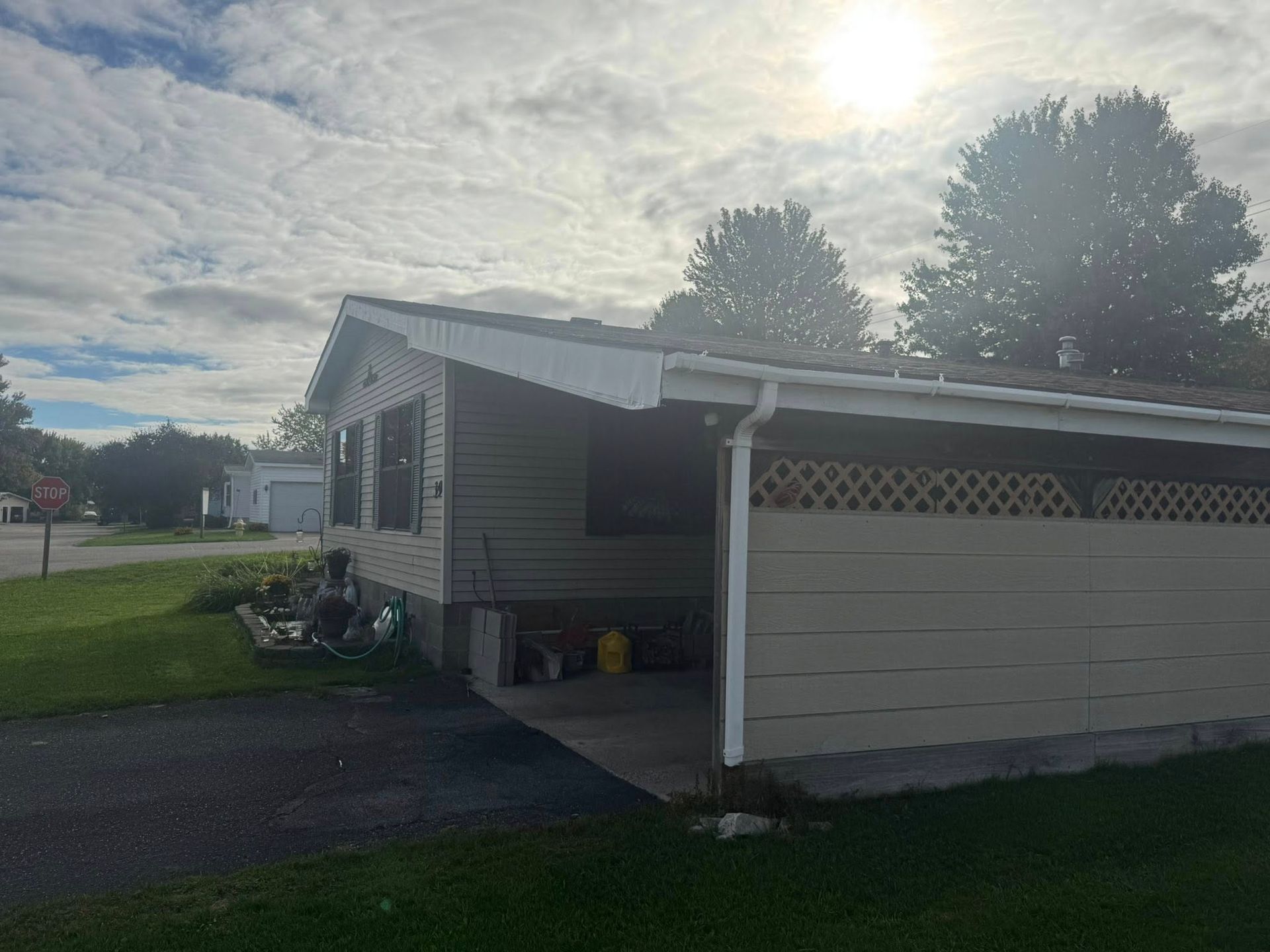 Small gray house with a carport, lawn, and bright sun overhead.