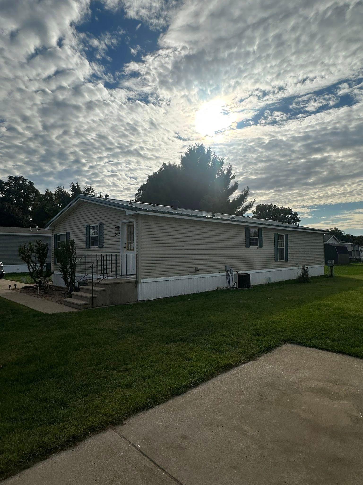 Single-story beige house with white trim under a cloudy sky, beside a green lawn and driveway.
